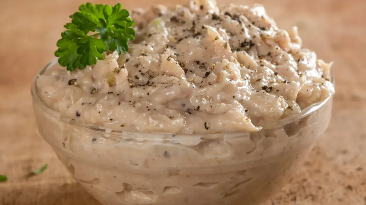 Pyszna pasta z tuńczyka w szklanej miseczce, doprawiona pieprzem i udekorowana gałązką natki pietruszki. Idealna na kanapki.