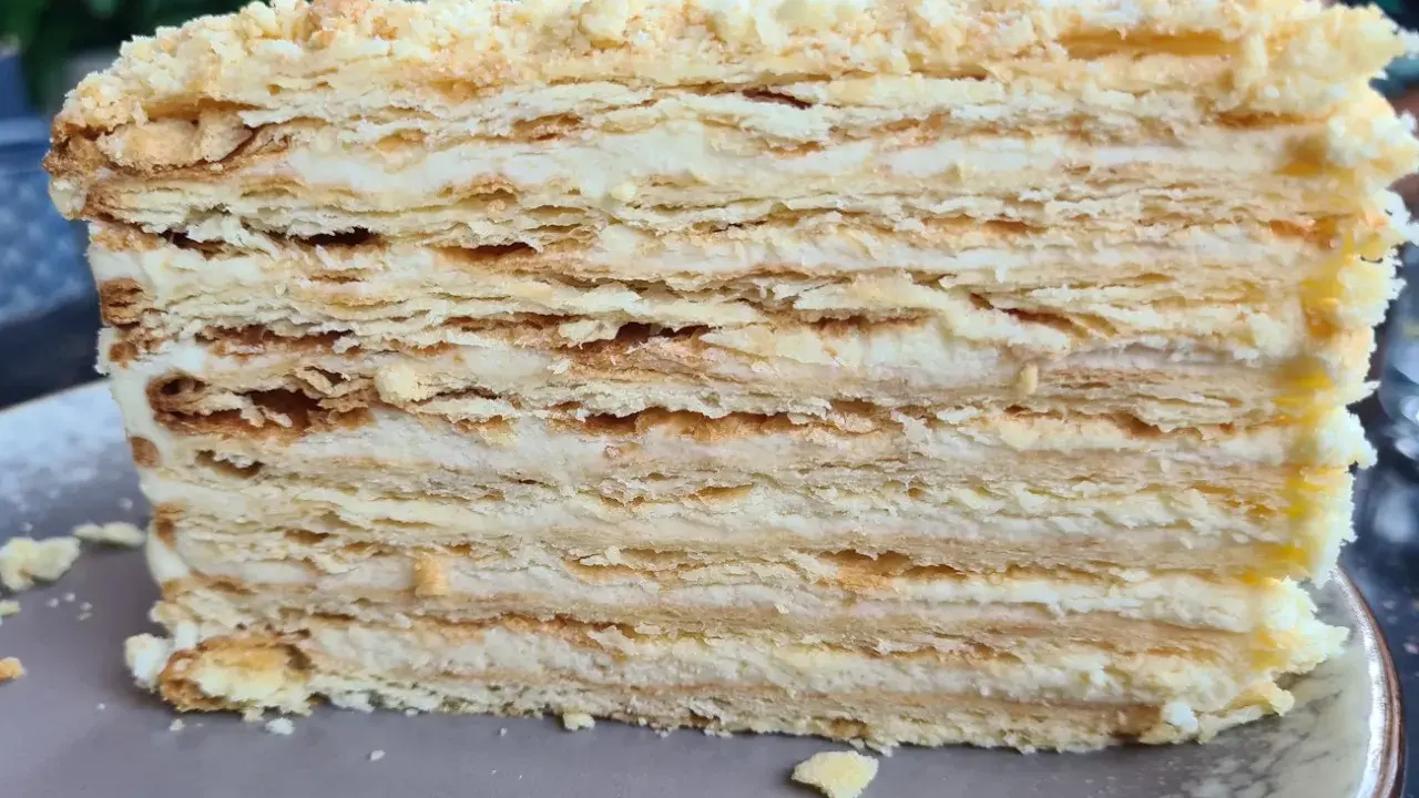 Warstwowe ciasto bez pieczenia z kremem. Kruche płatki ciasta przełożone delikatnym kremem, posypane okruszkami.