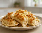 Pyszne pierogi ruskie, które Ania gotuje, polane skwarkami i posypane szczypiorkiem, na jasnym talerzu.