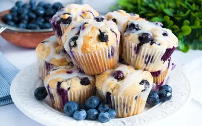 Stosik pysznych muffinek z borówkami, polanych lukrem, ozdobiony świeżymi owocami.
