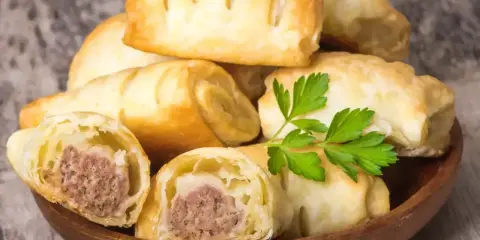 Stos pieczonego ciasta francuskiego z kiełbaską w środku, ozdobiony gałązką pietruszki.