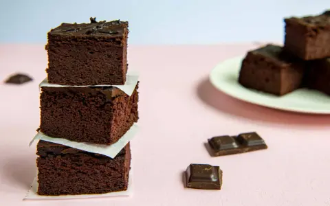 Ciemne, wilgotne brownie z fasoli, ułożone w wieżę, obok kawałków czekolady.
