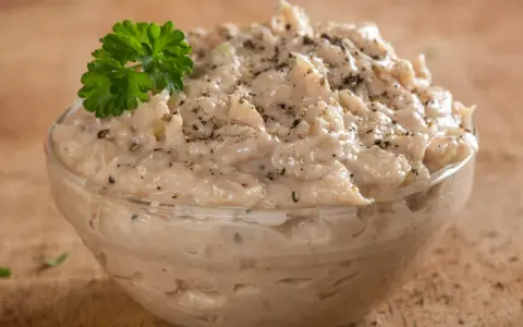 Pyszna pasta z tuńczyka w szklanej miseczce, doprawiona pieprzem i udekorowana gałązką natki pietruszki. Idealna na kanapki.