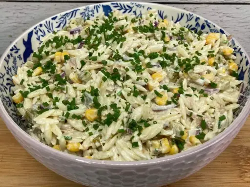 Pyszna sałatka z tuńczykiem, makaronem orzo, kukurydzą i szczypiorkiem, podana w ozdobnej misce.