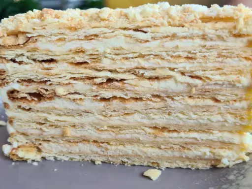 Warstwowe ciasto bez pieczenia z kremem. Kruche płatki ciasta przełożone delikatnym kremem, posypane okruszkami.