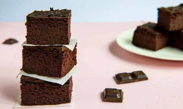 Ciemne, wilgotne brownie z fasoli, ułożone w wieżę, obok kawałków czekolady.