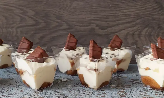 Słodkie deserki w pucharkach, przypominające tort Kinder Bueno, z kremem i kawałkami czekolady.