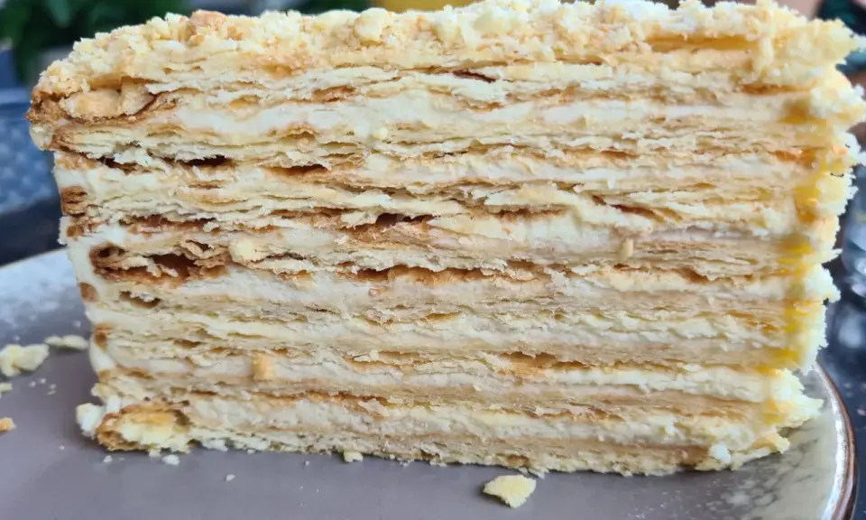Warstwowe ciasto bez pieczenia z kremem. Kruche płatki ciasta przełożone delikatnym kremem, posypane okruszkami.