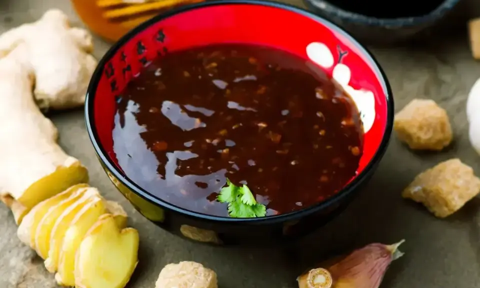 Sos teriyaki przepis: miseczka pełna aromatycznego sosu, obok świeży imbir, czosnek i brązowy cukier. Idealny do dań azjatyckich.
