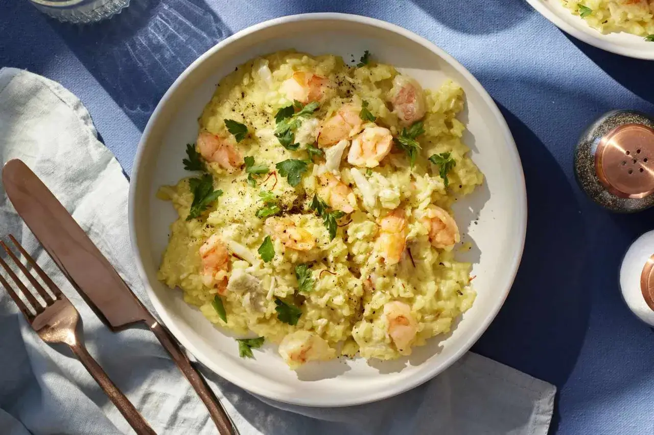 Kremowe risotto z krewetkami, ozdobione świeżą natką pietruszki i pieprzem. Idealne danie dla miłośnik&oacute;w owoc&oacute;w morza.