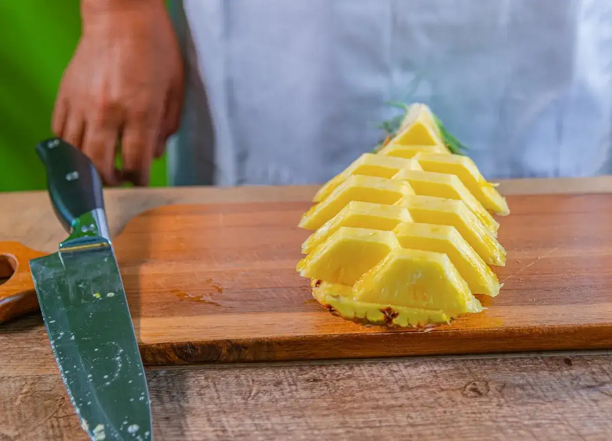 Pokrojony ananas na desce, obok n&oacute;ż. Proste wskaz&oacute;wki, jak pokroić ananasa, by cieszyć się jego smakiem.